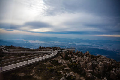 Boardwalk on mountain against cloudy sky