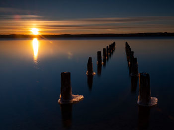 Wooden posts in lake against sky during sunset