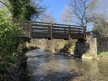 Bridge over river by trees against sky