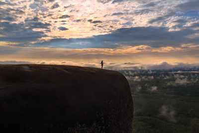 Mid distance of silhouette woman standing on mountain against cloudy sky during sunset