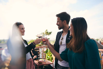 Smiling friends toasting drinks while partying on terrace