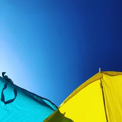 Low angle view of parasols against clear blue sky