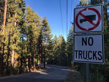 Warning sign by road amidst trees in forest