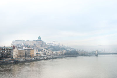 View of buildings by river against sky in city
