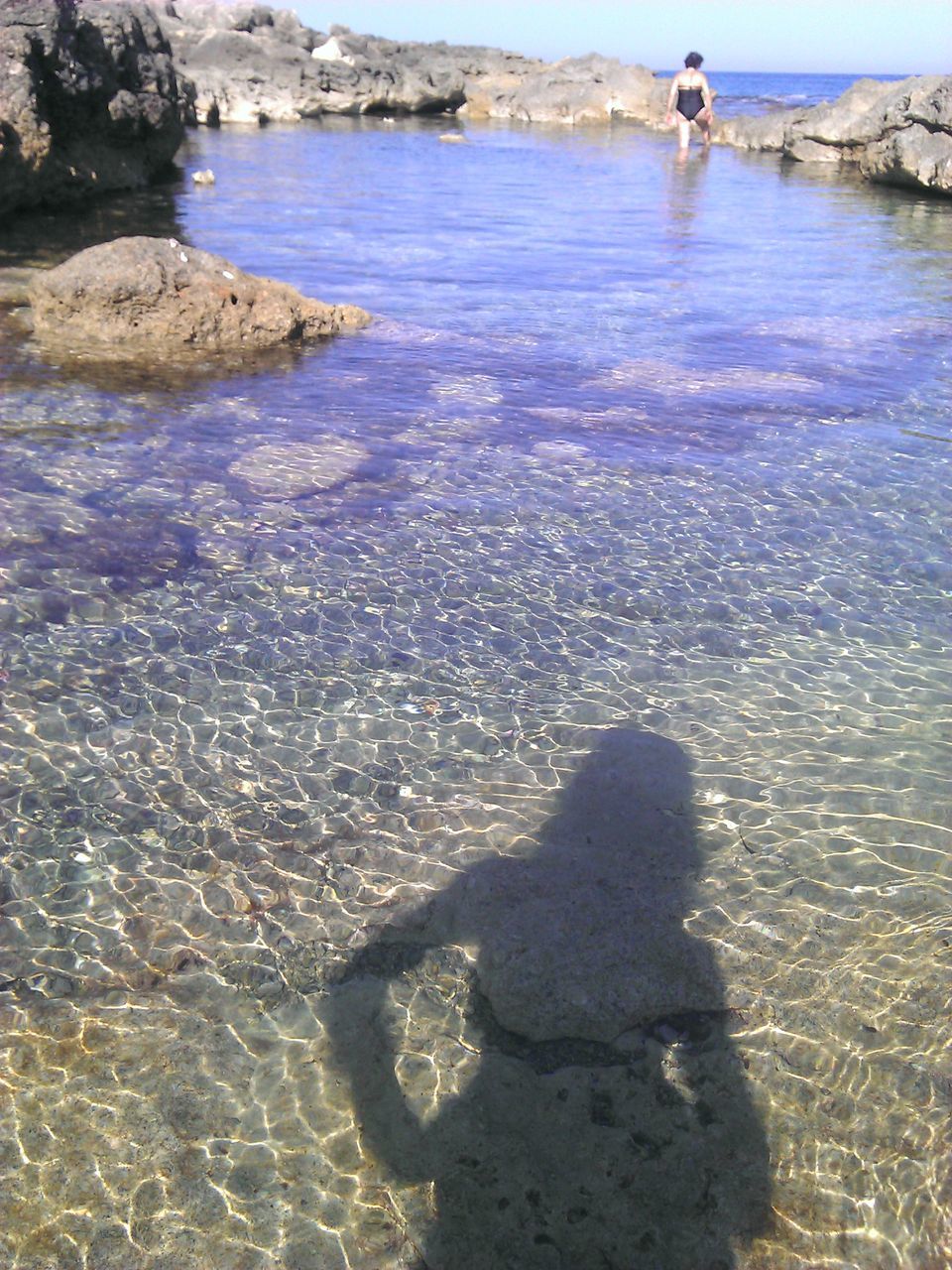 shadow, water, high angle view, leisure activity, beach, lifestyles, men, tranquil scene, sunlight, tranquility, unrecognizable person, scenics, sea, nature, beauty in nature, vacations, day, shore, person, focus on shadow, tourism, non-urban scene, city life, distant