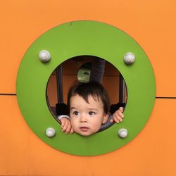 Cute baby boy looking through window of jungle gym in playground