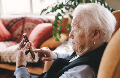 Senior woman sitting in the living room using smartphone