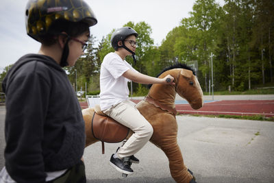 Boys having fun riding horse on wheels outdoors