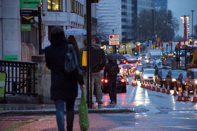 Rear view of people walking on street in city at dusk