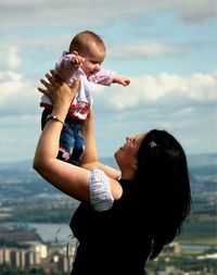 Mother lifting baby boy against sky