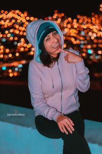 Full length of smiling young woman holding umbrella at night