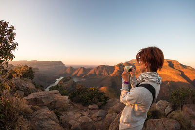 Woman photographing on rock against clear sky