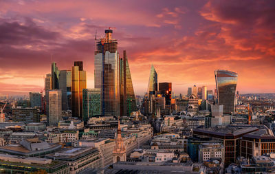 Modern buildings in city against dramatic sky during sunset