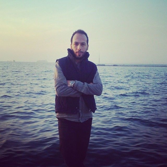 water, sea, lifestyles, young adult, leisure activity, waterfront, person, standing, young men, copy space, portrait, looking at camera, casual clothing, front view, clear sky, horizon over water, rippled, three quarter length