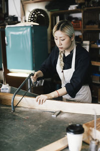 Young female entrepreneur cutting wood at workbench