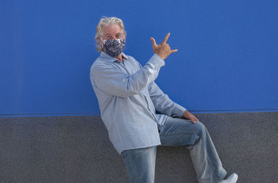 Portrait of man gesturing against blue wall