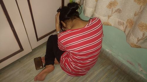 Rear view of depressed woman sitting on tiled floor at home