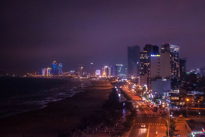 Illuminated street amidst buildings against sky at night