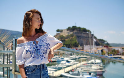 Young woman standing by railing against sky