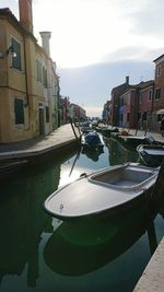 Boats moored in canal amidst city against sky