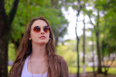 Beautiful young woman wearing sunglasses against trees