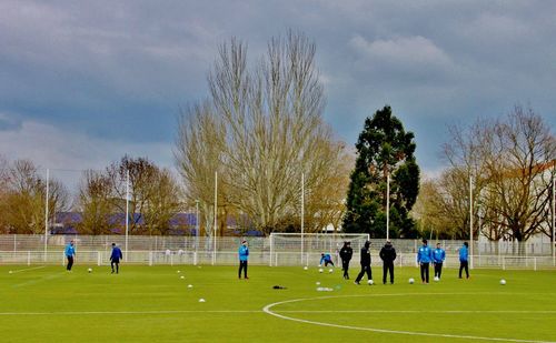 People at soccer field against cloudy sky