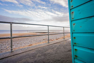 Metal railing by sea against sky