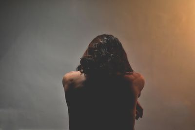 Rear view of shirtless young woman sitting against white wall