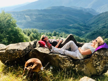 People relaxing on land against mountains