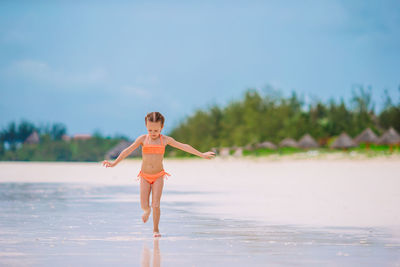 Full length of woman with arms raised on beach against sky