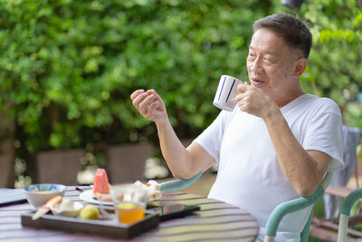 Smiling senior man drinking coffee while sitting on chair outdoors