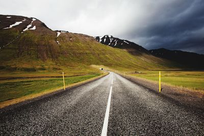 Empty road leading towards mountain against sky