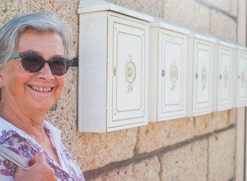 Portrait of smiling senior woman wearing sunglasses against wall