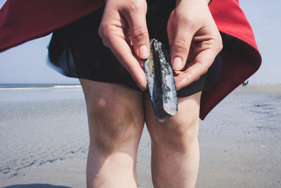 Midsection of woman holding shells while standing at beach