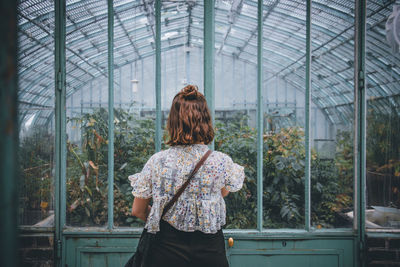 Rear view of woman standing in greenhouse