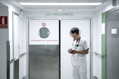 Pediatrician in white uniform with mobile phone standing in a corridor of clinic after end of work shift