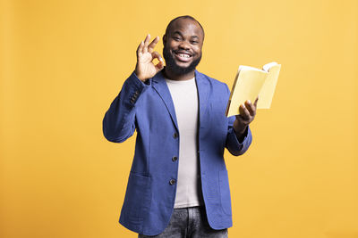 Portrait of young man standing against yellow background