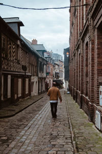 Rear view of man walking on footpath amidst buildings