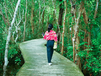 Rear view of woman walking on footpath amidst trees in forest