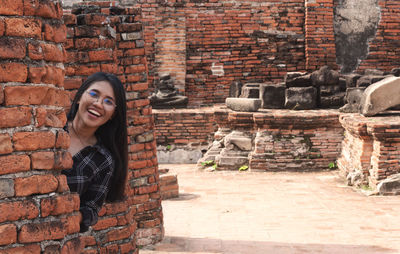 Portrait of smiling young woman against brick wall