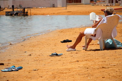 Woman reading book while sitting on chair at beach