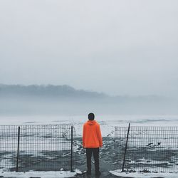 Rear view of man standing on snow covered landscape against sky