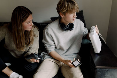 Teenage boy checking wi-fi router while sitting with friend on sofa at home