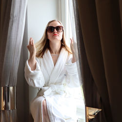 Young woman wearing sunglasses sitting on window