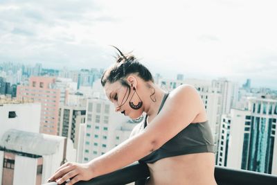 Close-up of young woman leaning on railing against city