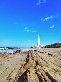 Lighthouse on beach against blue sky