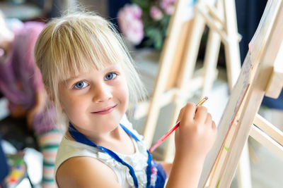 Portrait of smiling girl holding paintbrush indoors