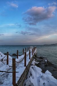 Wooden posts in sea against sky during winter