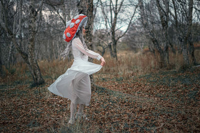 Woman standing by tree on field in forest