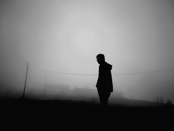 Silhouette man standing on field against sky during foggy weather